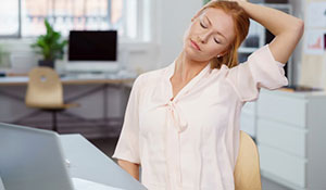 woman stretches neck at her desk