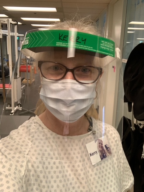 A physio poses in a facesheid, gown, mask and gloves